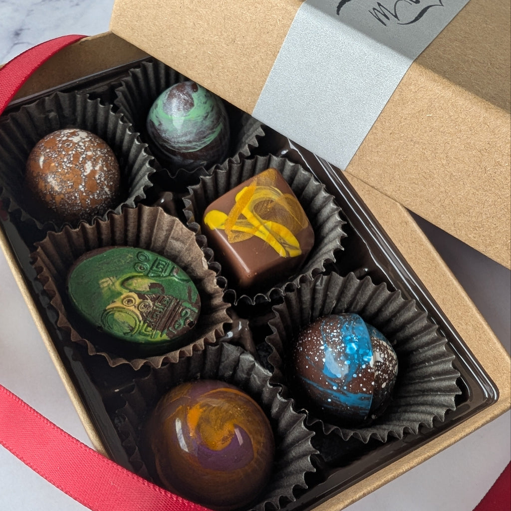 Box of hand painted chocolates with a red ribbon on a marble surface
