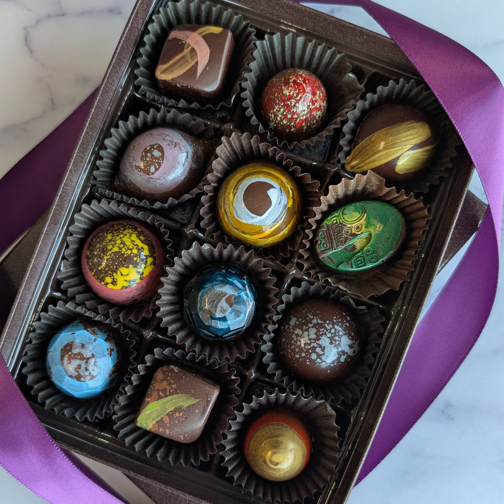Box of chocolates with colorful lids on a marble surface.  Handpainted chocolates